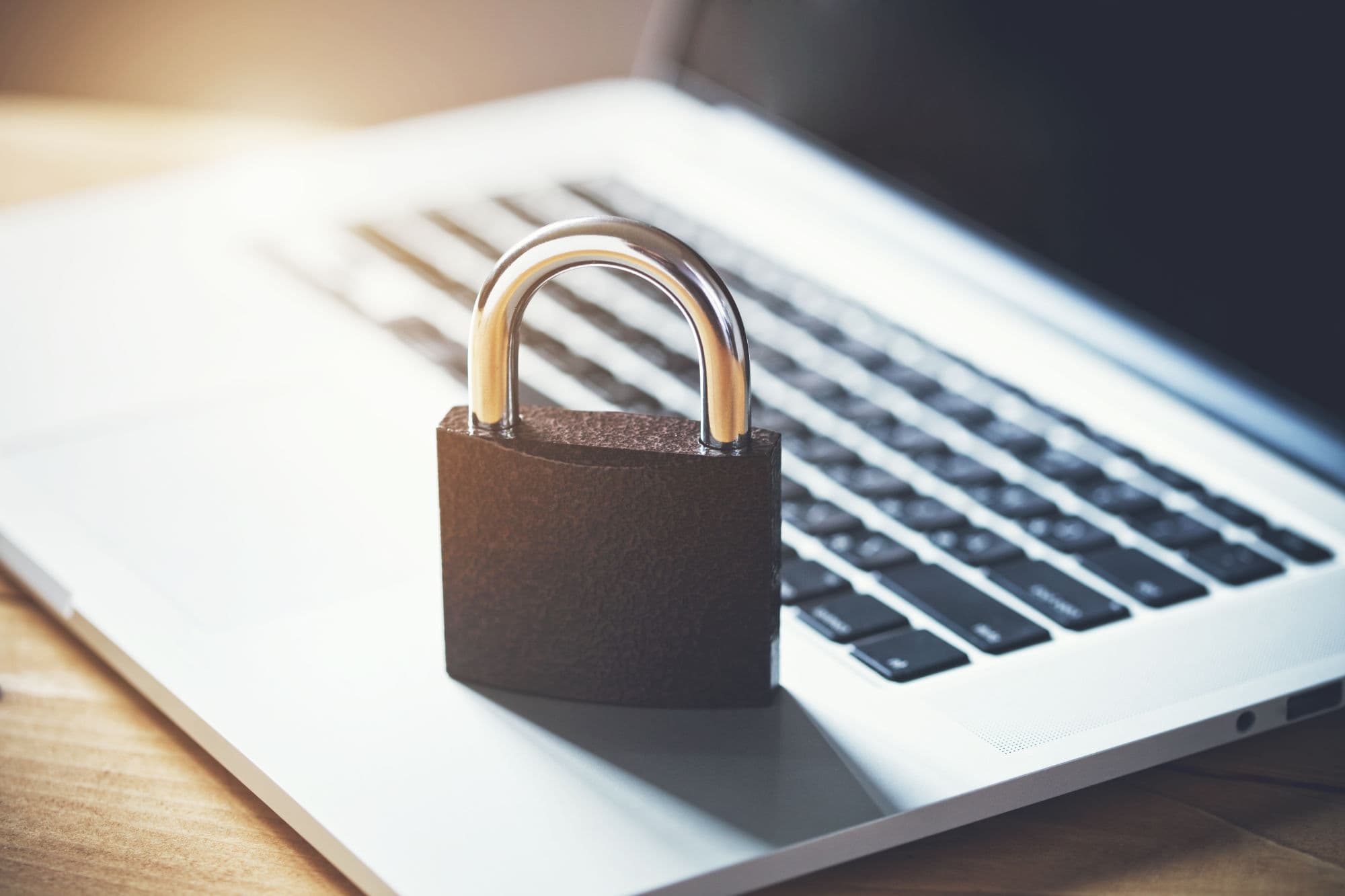 A Lock standing on an opened Laptop Computer with light shining from the back