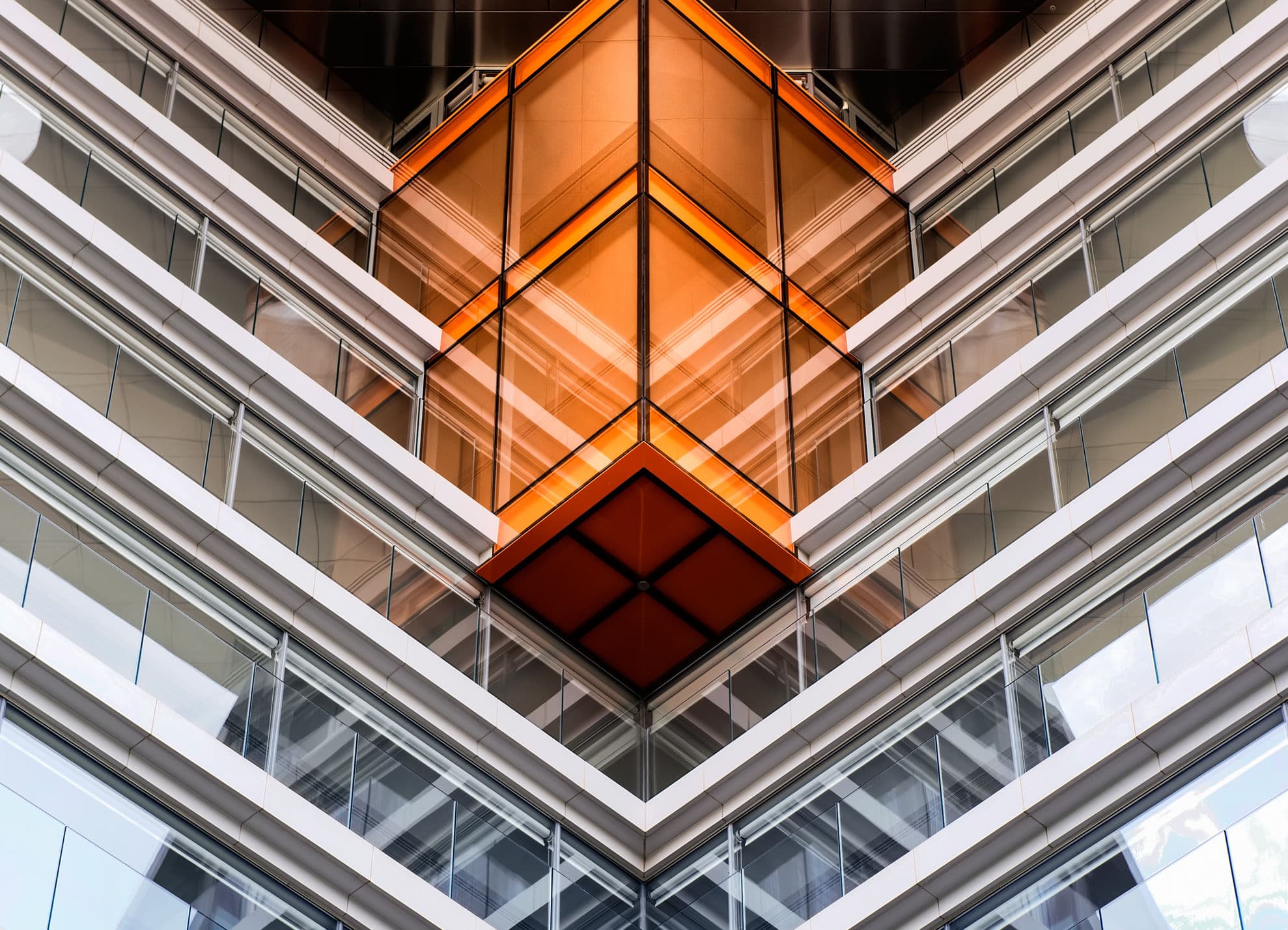 A modern glass building with sharp geometric lines and an orange illuminated section, creating a striking architectural perspective