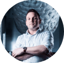 Jacco Besuijen standing with arms crossed, wearing a white shirt, with a modern industrial background