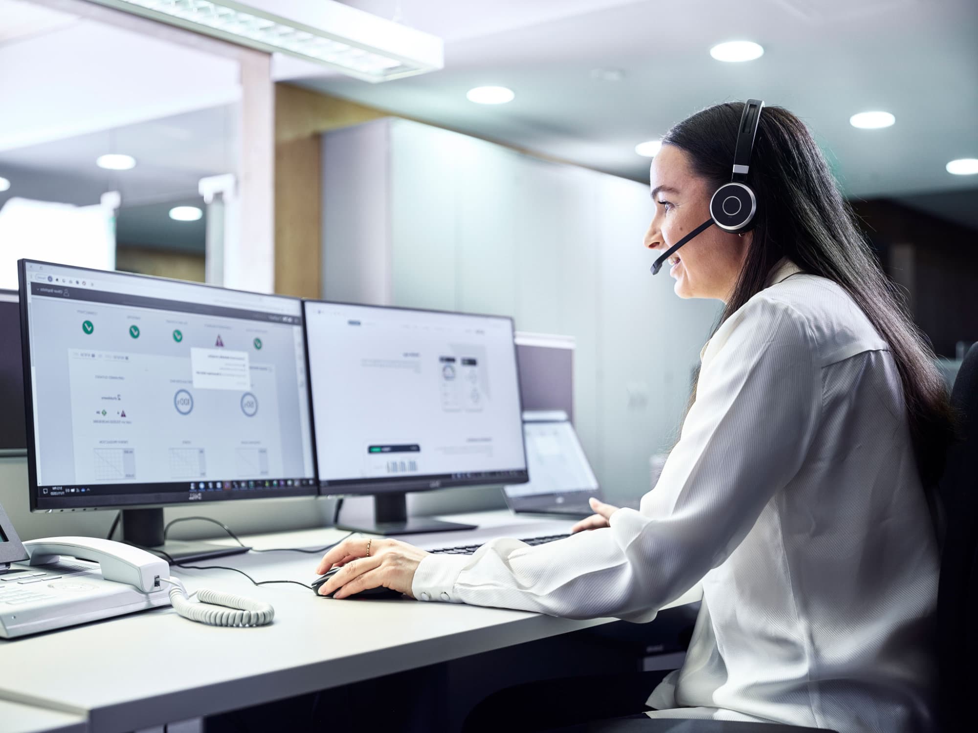 a Woman is sitting in front of two Computerscreens and looking at one screen